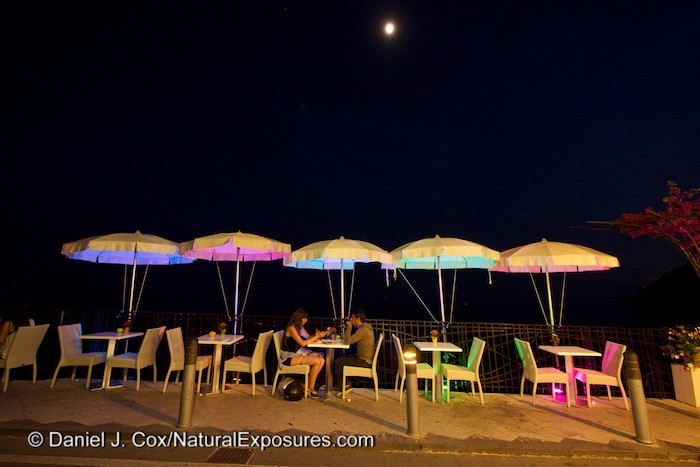 A young Italian couple enjoy a romantic dinner and the warm evening air under the colored umbrellas along the coast of Positano, Italy