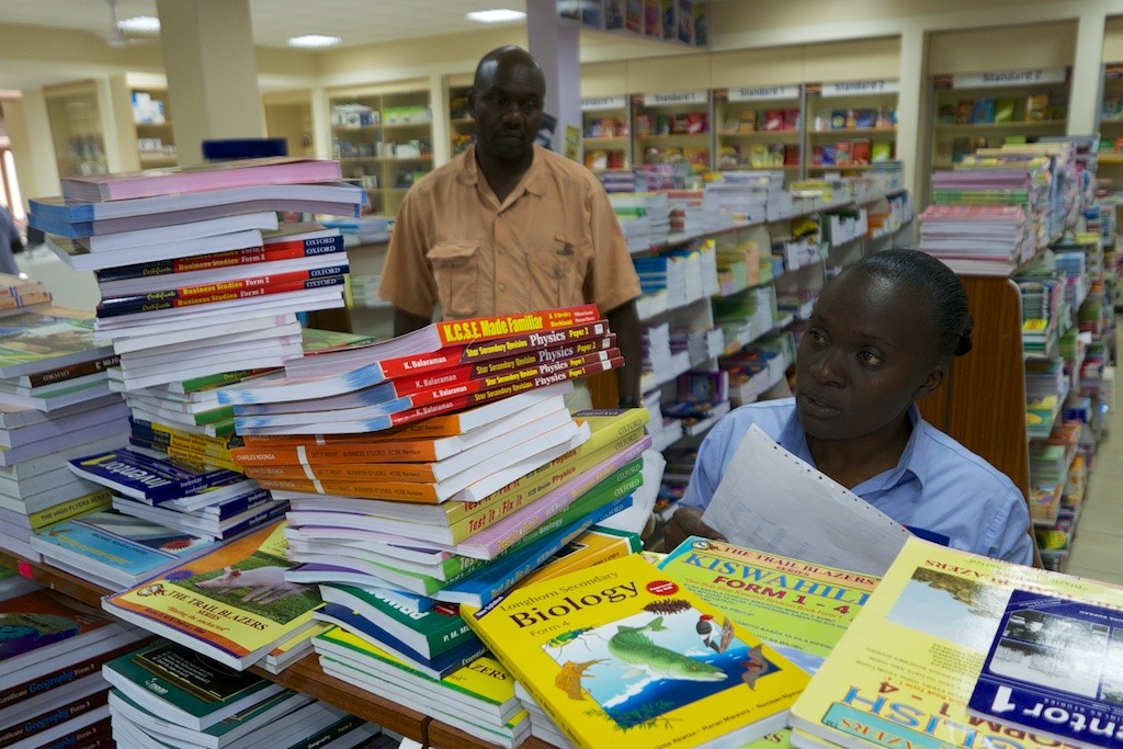 Nairobi Text Book store clerk with Henry Miwani searches the many thousands of books to gather the titles we need for the Natural Exposures Text Book Project. Nairobi. Kenya. Lumix LX100