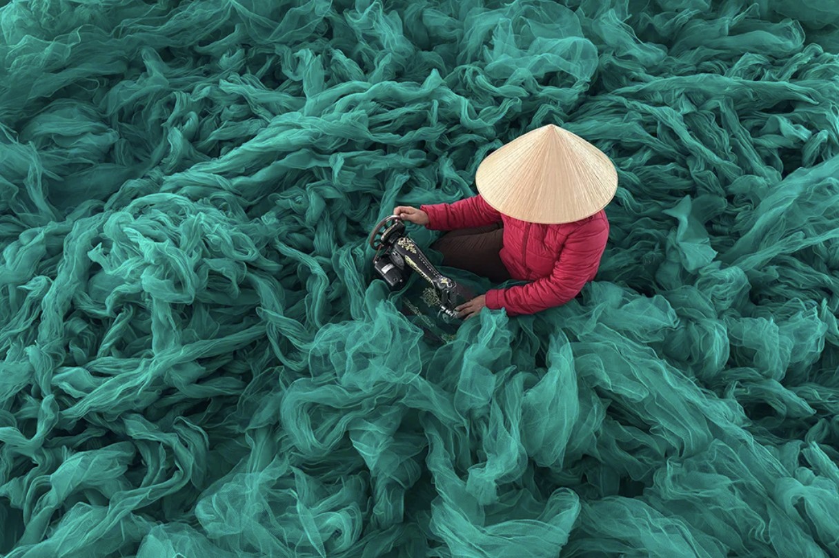 Vietnamese worker in a conical hat surrounded by turquoise fishing nets